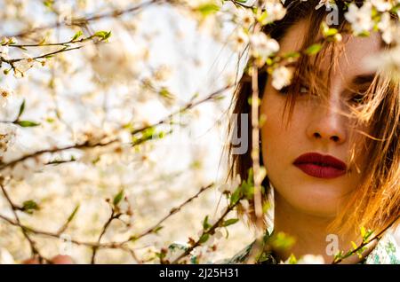 Belle fille blonde souriante posant dans des fleurs de pêche à l'extérieur. Banque D'Images