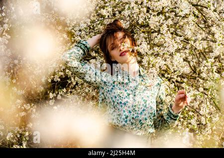 Belle fille blonde souriante posant dans des fleurs de pêche à l'extérieur. Banque D'Images