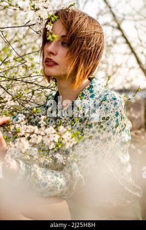 Belle fille blonde souriante posant dans des fleurs de pêche à l'extérieur. Banque D'Images