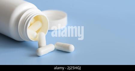 Pilules blanches dispersées dans un contenant de médecine en plastique blanc Banque D'Images