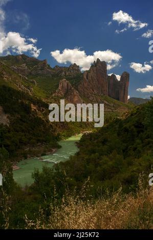 Les ombres nuages assombrissent les pentes accidentées au-dessus des eaux vert clair du Rio Gallego, tandis qu'il s'élève sous les majestueux Mallos de Riglos, une passerelle naturelle spectaculaire vers les Pyrénées. Los Mallos (les maillets), dans la province de Huesca, Aragon, Espagne, ont au moins 20 millions d'années. Ils s'élèvent à environ 300 m (980 pi), formant une frontière physique entre les contreforts pyrénéens et le bassin de l'Ebre. Banque D'Images