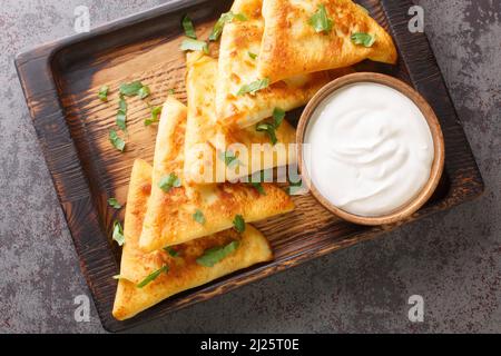 Délicieux chaussons ukrainiens benderyki avec de la viande servi avec de la crème aigre gros plan sur un plateau en bois sur la table. Vue horizontale du dessus Banque D'Images