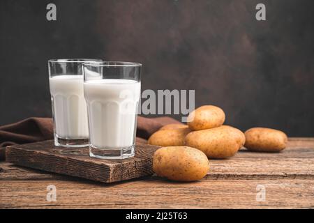 Lait de pomme de terre vegan en deux verres et pommes de terre sur fond marron. Banque D'Images