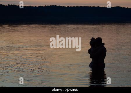 Couple amoureux d'avoir des moments romantiques tendres au coucher du soleil. Les amoureux de lune de miel qui s'embrasent sur la plage. Silhouettes de couple contre le ciel du coucher du soleil. Banque D'Images