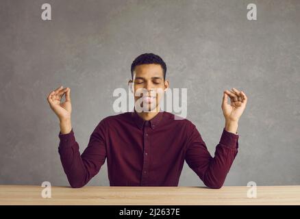 Heureux calme jeune latin homme méditant avec les yeux fermés souriant assis à la table. Banque D'Images