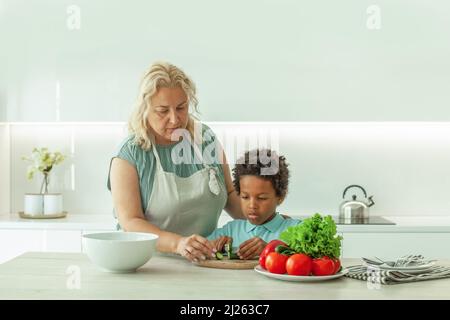 Mère et enfant sérieux concentré coupant le concombre à l'intérieur de la cuisine Banque D'Images