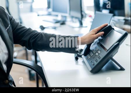 Gros plan main féminine sur téléphone fixe au bureau. Une femme sans visage en costume fonctionne comme une réceptionniste répondant au téléphone aux appels des clients. Banque D'Images