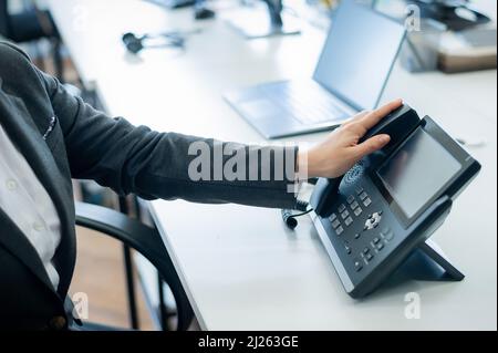 Gros plan main féminine sur téléphone fixe au bureau. Une femme sans visage en costume fonctionne comme une réceptionniste répondant au téléphone aux appels des clients. Banque D'Images