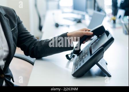 Gros plan main féminine sur téléphone fixe au bureau. Une femme sans visage en costume fonctionne comme une réceptionniste répondant au téléphone aux appels des clients. Banque D'Images