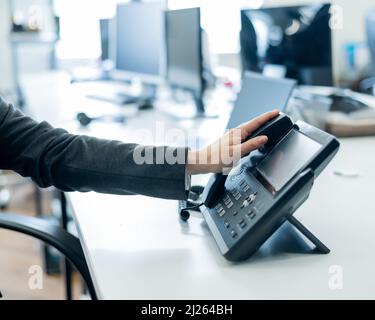 Gros plan main féminine sur téléphone fixe au bureau. Une femme sans visage en costume fonctionne comme une réceptionniste répondant au téléphone aux appels des clients. Banque D'Images