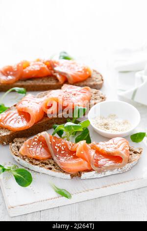 Pain de seigle complet sandwichs ouverts avec saumon salé sur une table en bois rustique blanc. Une alimentation saine Banque D'Images