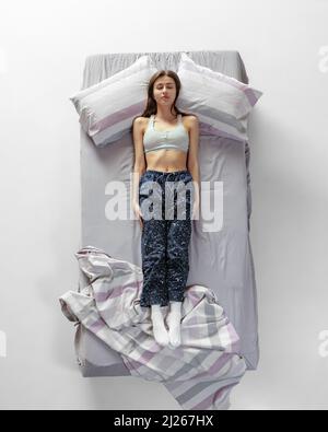 Vue de dessus portrait de jeune fille portant des vêtements de maison, pyjama dormant dans un grand lit gris. Concept de santé, intérieur de maison, temps de détente, famille, rêves Banque D'Images