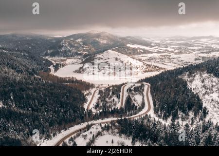 Vue aérienne de drone sur les montagnes d'hiver avec route de montagne en serpentin, rivière et forêt. Photographie de paysage Banque D'Images