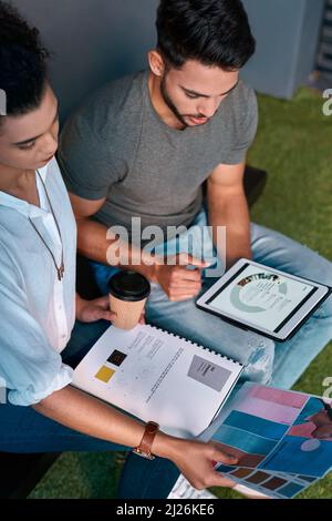 Comparons les données. Prise de vue rognée de deux jeunes collègues d'affaires assis ensemble et à l'aide d'une tablette tout en lisant des documents. Banque D'Images