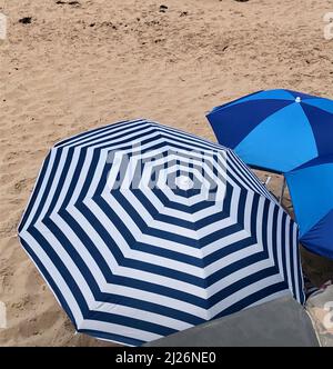 parapluie de plage à motif rayé et parapluie de plage bleu deux tons dans le sable sur un être Banque D'Images