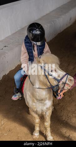 un garçon méconnaissable qui fait du poney blanc, des leçons d'équitation Banque D'Images