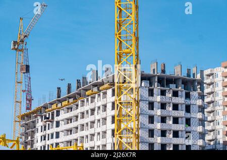 Construction d'un bâtiment à plusieurs étages.grues jaunes et bleues. Lumière du soleil sur le chantier. Banque D'Images