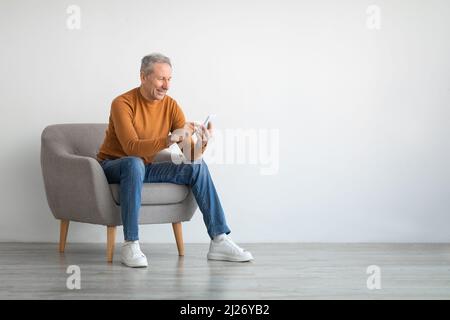 Portrait d'un homme mûr avec un smartphone assis sur un fauteuil Banque D'Images