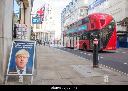 Un bus à impériale passe devant une pancarte à laquelle le Premier ministre britannique Boris Johnson est présent devant un magasin de cartes de vœux dans le centre de Londres. Banque D'Images