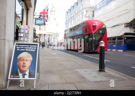 Un bus à impériale passe devant une pancarte à laquelle le Premier ministre britannique Boris Johnson est présent devant un magasin de cartes de vœux dans le centre de Londres. Banque D'Images