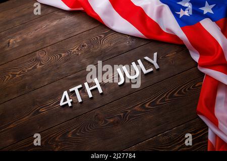 les mots 4th juillet et drapeau américain froissé sur fond plat texturé de surface en bois. Banque D'Images