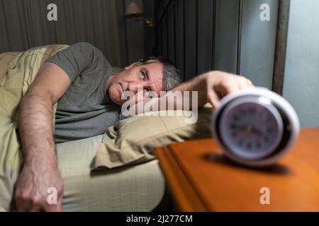 Homme souffrant d'insomnie couché au lit avec horloge sur la table de chevet. Banque D'Images