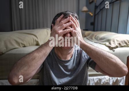 Homme souffrant d'insomnie assis sur le sol et avec ses mains sur son visage dans le désespoir. Banque D'Images
