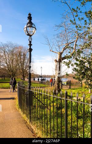 Les gens qui marchent à côté d'un lampadaire à l'ancienne sur le sentier à côté du lac Serpentine à Hyde Park, Londres, lors d'une journée d'hiver ensoleillée et lumineuse. Banque D'Images