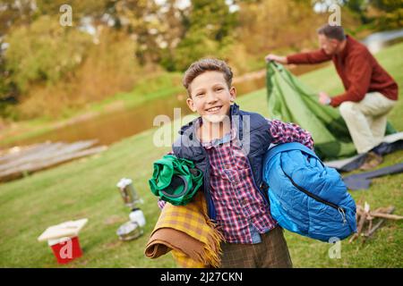 Tout sauf l'évier de cuisine. Portrait d'un jeune garçon tenant du matériel de camping avec son père en arrière-plan. Banque D'Images