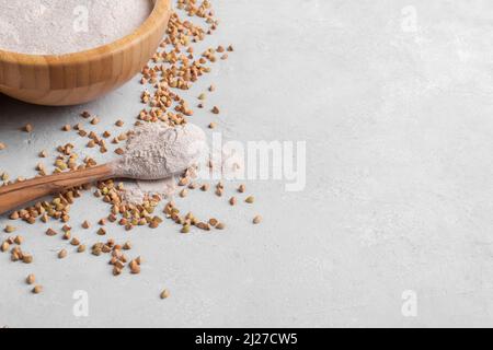 Farine de sarrasin en cuillère en bois et bol avec grain de sarrasin vert brut sur fond de pierre gris clair, gros plan, vue du dessus. Farine alternative, gluten Banque D'Images