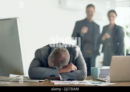 Tirer quelqu'un vers le bas ne vous aidera pas à atteindre le sommet. Coup de feu d'un homme d'affaires abattu allongé sur ses bras à son bureau tandis que ses collègues le moquent dans le Banque D'Images