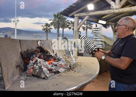 Homme grill des sardines (Espetos) sur le feu à l'extérieur du restaurant à Malaga Andalousie Espagne. Banque D'Images