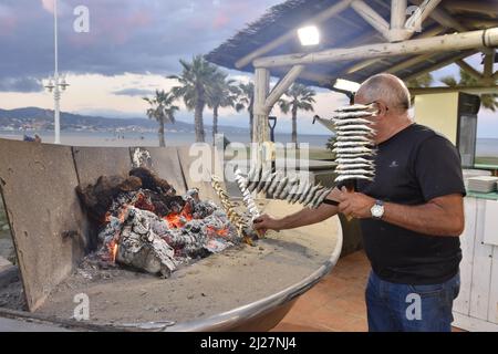 Homme grill des sardines (Espetos) sur le feu à l'extérieur du restaurant à Malaga Andalousie Espagne. Banque D'Images