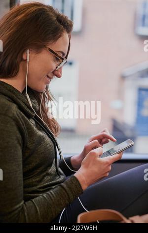 Vérification des lignes de bus en ligne. Prise de vue rognée d'une jeune femme attrayante écoutant de la musique tout en étant assise dans un bus. Banque D'Images