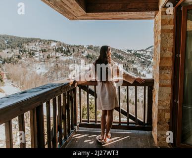 Vue arrière de la charmante jeune femme en peignoir profitant de la nature hivernale sur la grande terrasse Banque D'Images