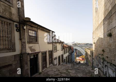 Porto, Portugal. Mars 2022. Une rue typique entre les vieilles maisons du centre-ville qui descend vers la rivière avec le Dom Luís i Iron brid Banque D'Images