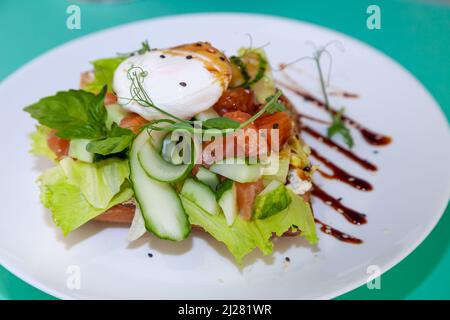 Griller avec du saumon et de l'œuf poché. Laitue, concombre, basilic. Un sandwich santé pour le petit déjeuner. Graines de Microgreen et de lin et de sésame. Aliments sains sur une assiette blanche. Poisson avec légumes sur le pain. Banque D'Images