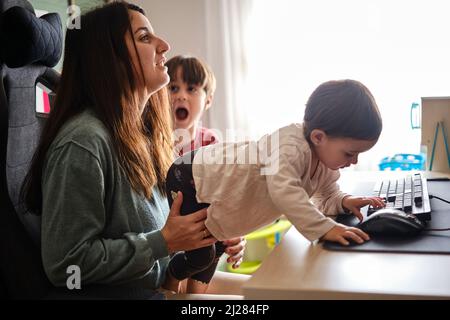 Mère essayant de travailler à distance de la maison tout en prenant soin de ses enfants. Banque D'Images