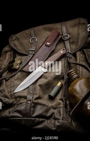 Couteau de chasse avec poignée en bois sur un sac à dos en toile vintage. des obus de fusil de calibre 12 et une cantine d'eau sont à proximité. Ensemble Hunter's. Fond noir Banque D'Images