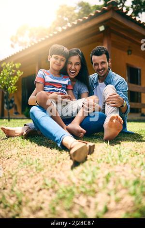 Peu importe où nous sommes, tant que nous étions ensemble. Portrait en longueur d'une jeune famille heureuse de trois personnes, assise sur leur pelouse dans l'arrière-cour. Banque D'Images