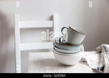 Une pyramide de bols blancs, assiettes et tasses de différentes tailles et couleurs sur une table beige dans la cuisine.Style scandinave.Place pour votre texte.Copier Banque D'Images