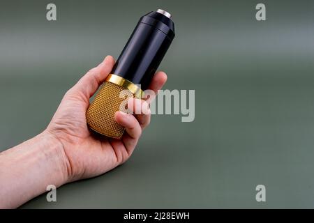 Main tenant un microphone doré et noir avec un arrière-plan verdâtre. Banque D'Images