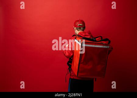 Liveur en uniforme rouge avec un sac à dos thermique isolé sur un fond blanc.Livraison rapide à domicile.Commande en ligne.Le service de messagerie livre les articles d'épicerie à la Banque D'Images