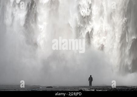 Puissante et massive cascade de Skogafoss avec homme debout devant et très proche, sud de l'Islande Banque D'Images