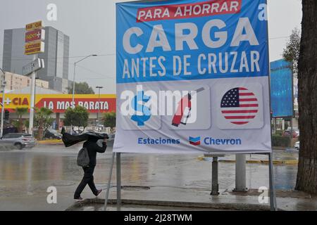 Imperial Beach, Californie, États-Unis. 28th mars 2022. Un homme marche pendant une tempête en passant devant une publicité pour un gaz moins cher à Tijuana, au Mexique, destinée aux touristes américains qui veulent économiser à la pompe avant de traverser la frontière entre les États-Unis et le Mexique le lundi 28 mars 2022. (Image de crédit : © Carlos A. Moreno/ZUMA Press Wire) Banque D'Images