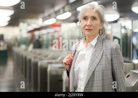 Femme européenne mûre debout près des barrières tarifaires dans la station de métro. Banque D'Images