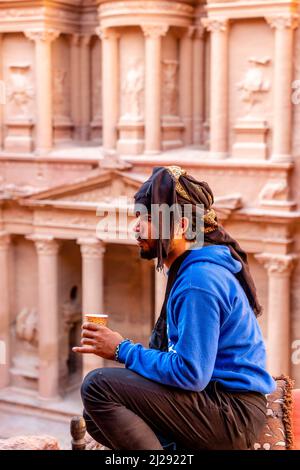 Un guide bédouin local assis en buvant du café Ovelooking l'extérieur du Trésor "Al-Khazneh", d'Un point de vue élevé, Petra, Jordanie, Asie. Banque D'Images