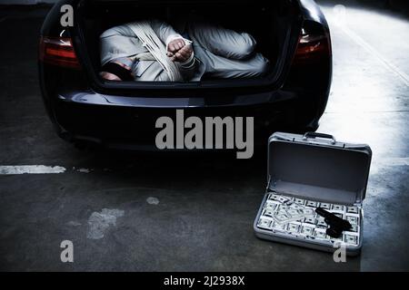 L'argent par la violence. Un homme d'affaires lié et aveuglés allongé dans le coffre d'une voiture à côté d'une mallette de rançon d'argent. Banque D'Images