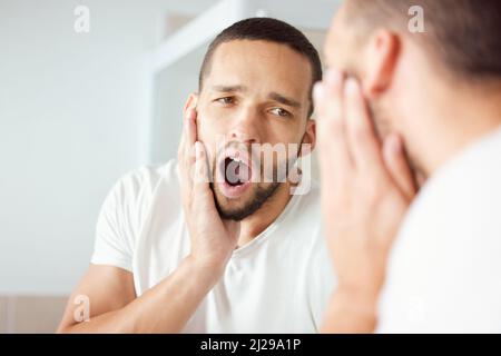 Se réveiller très tôt aujourd'hui était très serviable. Photo d'un jeune homme bâillant en regardant son reflet dans le miroir de la salle de bains. Banque D'Images