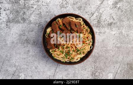 Soupe de nouilles de bœuf épicée aux herbes dans un bol sur fond gris foncé. Vue de dessus, plan d'appartement Banque D'Images